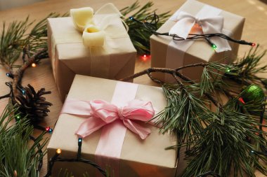 Noel hediyesi kağıdında pembe kurdele, çam dalı ve tahta masada duran Noel oyuncakları.