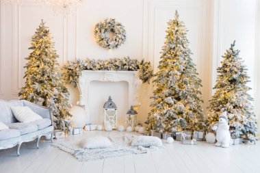 Şömineli beyaz bir oda, yapay kar ve çelenkli Noel ağaçları, bir kanepe, yastıklı bir ekose, fenerli bir beyaz oyuncak ayı, içinde yılbaşı hediyeleri olan kutular, bir çelenk.