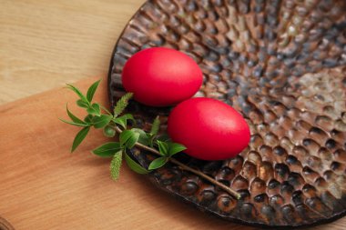 Kırmızı Paskalya yumurtaları ve yeşil bir dal, tahta masanın üzerindeki kesme tahtasının üzerinde duruyor.