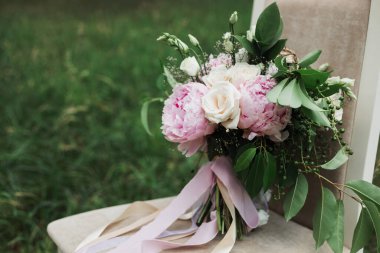 Baharda açık havada zarif, narin bir düğün buketi parktaki çimlerin üzerinde bir sandalyenin üzerinde duruyor ağaçların, güllerin, şakayıkların, yeşilliklerin, çiçeklerin, çiçeklerin, böğürtlenlerin, kurdelelerin arka planında