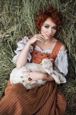 Ulusal Bavyera kostümlü kızıl saçlı kadın gülümser ve bir çocuğu samanlıkta elinde tutar, oktoberfest