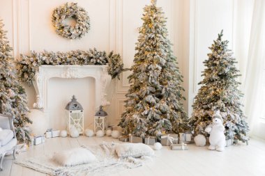 Şömineli beyaz bir oda, yapay kar ve çelenkli Noel ağaçları, bir kanepe, yastıklı bir ekose, fenerli bir beyaz oyuncak ayı, içinde yılbaşı hediyeleri olan kutular, bir çelenk. 