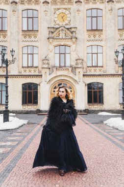 Gece makyajı ve saç stili ile güzel sarışın kadın, kırmızı dudaklar, retro kıyafetler, mavi uzun elbise, guipure eldivenler ve siyah silindir şapka, kürk pelerin, eski bir binanın yanında duruyor, kış, kar,