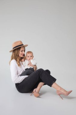 Stüdyoda yerde oturan anne ve çocuğun moda portresi. Kızıyla birlikte genç bir kadın.