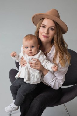 Stüdyoda sandalyede oturan güzel anne ve kız, sıradan bir aile görünüşü.