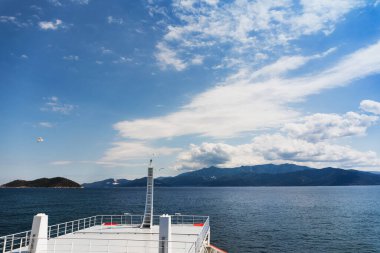 Yunanistan 'da turist macerası rengarenk yaz manzarası, feribotun yanından manzara, açık deniz mavi su, martılar, ada, dağlar, orman, bulutlu mavi gökyüzü