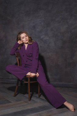 Sandalyede oturan takım elbiseli bir kadının stüdyo portresi.  