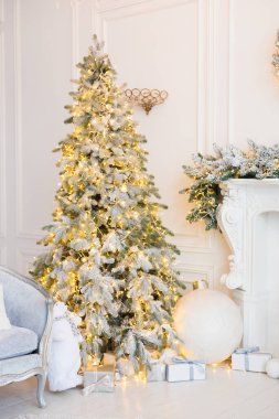 Şömineli beyaz bir oda, yapay kar ve çelenkli Noel ağaçları, bir kanepe, yastıklı bir ekose, fenerli bir beyaz oyuncak ayı, içinde yılbaşı hediyeleri olan kutular, bir çelenk. 