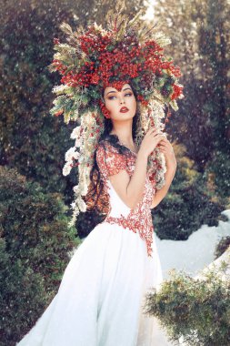 Kırmızı böğürtlen ve dallardan oluşan taç giymiş güzel bir kadın ormandaki düşen karların arasında duruyor.