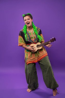 Açık yeşil saçlı, ukulele çalan hippi kadının stüdyo portresi.