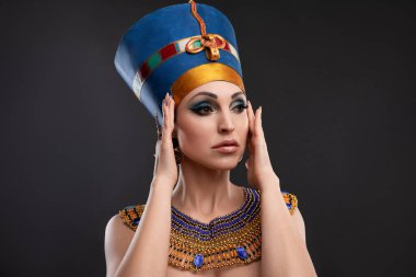Kraliçe Kleopatra, taç, kolye görünümünde kahverengi gözlü ve akşam makyajlı güzel bir kadının yakın plan stüdyo portresi.