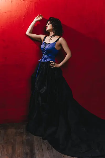 一位美丽的黑发女子站在靠近红墙的木地板上 她身穿黑色和紫色紧身衣 头戴大钻石项链 晚上化妆 一头卷曲的发式 — 图库照片