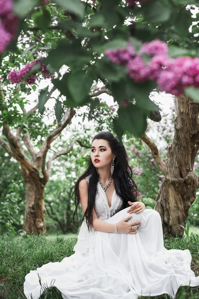 春天的户外画像 一个美丽性感的黑发女人站在樱桃树下 她的花朵 长长的白衣 夜晚的妆容 — 图库照片