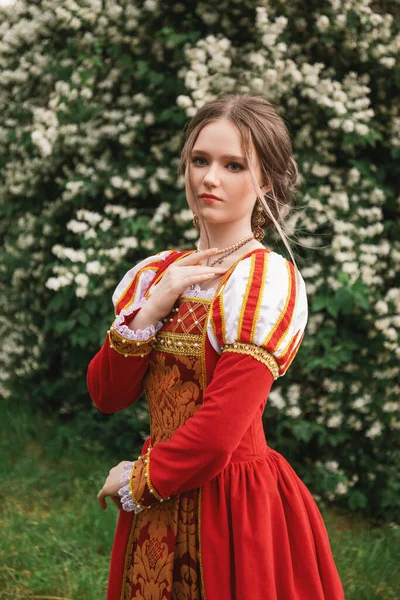 Piękna Młoda Kobieta Czerwonej Średniowiecznej Sukience Stoi Ogrodzie Białych Kwiatach — Zdjęcie stockowe