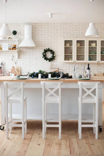 the interior of the modern kitchen in bright colors, a bar counter and three bar stools, Christmas decorations, cutlery, a brick wall, an extractor fan, white and beige color