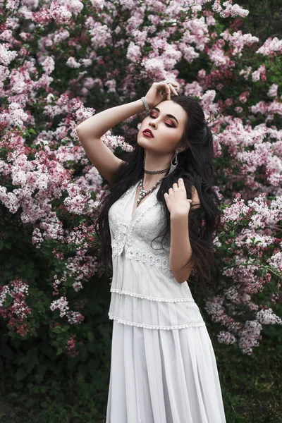 紫丁香花中美丽性感的黑发女子的春天户外肖像 长长的白色连衣裙 — 图库照片