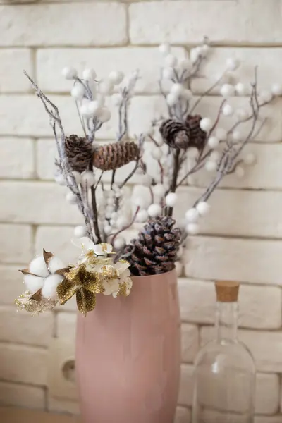 厨房桌子上靠墙立着一只粉色花瓶 上面挂着一束鲜花 树枝上挂着球果 棉花和金花 闪闪发光 还有一只透明的瓶塞 — 图库照片