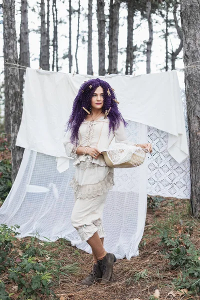 紫色のカーリーヘアが付いているブーホー様式の服の美しい女性は森 自然の生命 生きている環境で乾燥するために衣服を掛けます — ストック写真