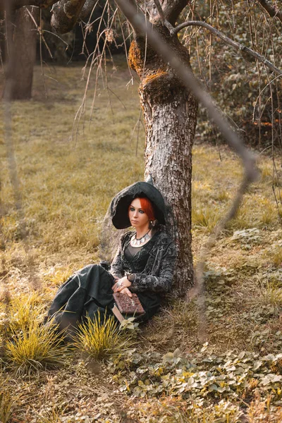 穿着黑色衣服的红头发女巫婆 秋天公园里戴着尖尖的帽子 笑着穿万圣节服装 — 图库照片
