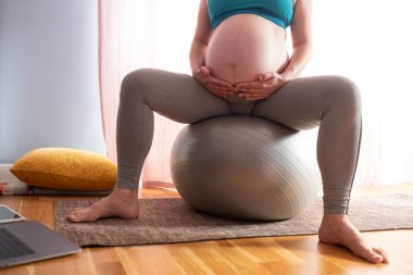 Genç hamile, beyaz kadın evde yoga yapıyor. Dizüstü bilgisayarda lessong.