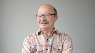 Beyaz arka planda duran gözlüklü, gülümseyen olgun bir adamın portresi..