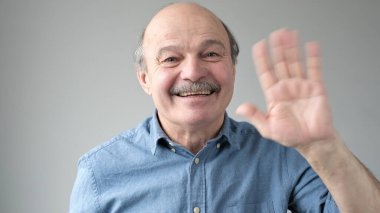 Arkadaş canlısı görünümlü çekici Avrupalı emekli neşeli bir şekilde gülümserken el sallayarak selam veriyor. Büyükbaba torununa hoş geldin diyor. Seni gördüğüme çok sevindim..