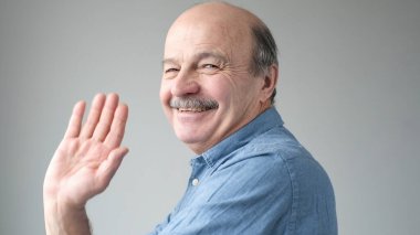 Arkadaş canlısı görünümlü çekici Avrupalı emekli neşeli bir şekilde gülümserken el sallayarak selam veriyor. Büyükbaba torununa hoş geldin diyor. Seni gördüğüme çok sevindim..
