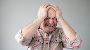 Kafkasyalı kıdemli bir adam başının ne kadar ağrıdığını gösteriyor, acı çekiyor, perişan ve bitkin görünüyor.