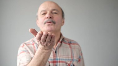 Orta yaşlı kel bir adam hava öpücüğü veriyor. Gri arka planda izole edilmiş kapalı stüdyo görüntüleri..