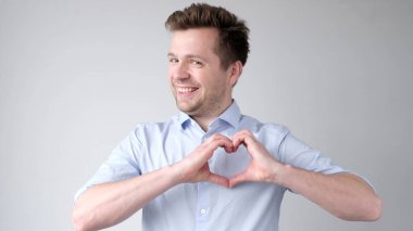 European young man shows a heart sign and confesses love. Studio shot clipart