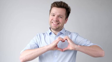 European young man shows a heart sign and confesses love. Studio shot clipart