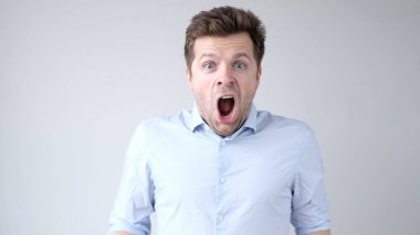 European young man is greatly surprised and opens his mouth in astonishment. Studio shot clipart
