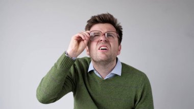 European young man with poor vision peers through his glasses, trying to discern the information that interests him. Studio shot clipart