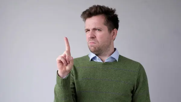 stock image European young man shakes his head in disagreement and says no, pointing his finger upwards. Studio shot
