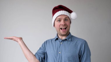 Yeni yıl şapkalı neşeli Avrupalı genç adam bir ürünü sunan boş bir alanı işaret ediyor. Stüdyo çekimi