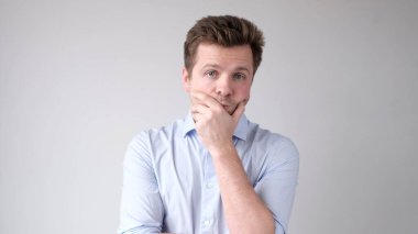 Genç bir adam düşünceli bir şekilde kameraya bakıyor, zor bir seçimle kafası karışmış.