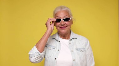 An elderly European woman in glasses confidently looks into the camera, smiling. Studio shot clipart