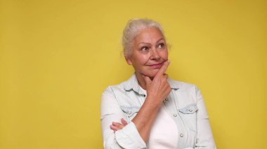 Elderly European woman is lost in thought, dreaming, and scratching her chin with her finger. clipart