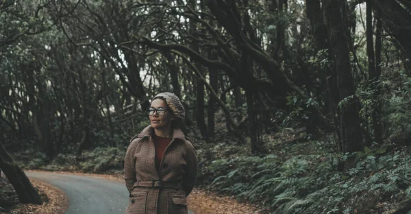 stock image woman walking in the green forest woods on road with trees around enjoying nature and environment national park. Winter outdoor leisure activity with female people tourist enjoying scenic place