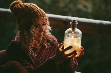 Day dreaming concept emotion and activity with adult woman holding and looking an old bottle with warm lights inside in outdoor. Winter season. Dreamer lifestyle. Future goals and plans people clipart