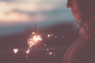 Pırıltılı ışık, kutlama konsepti, duygu ve aktivitenin yanı sıra, gülen ve akşamları tek başına kutlama yapan mutlu bir kadının görüntüsü. Renkli bir karanlık arka plan. İnsanlar yalnız kutluyor