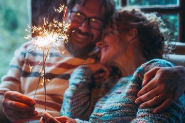 Evde birbirine aşık romantik bir çift gecenin karanlığında havai fişek ışığıyla birbirlerine sarılıp gülümsüyorlar. Yeni yıl ve yıldönümü etkinliği konsepti. Erkek ve kadın kutlama ilişkisinin tadını çıkarır