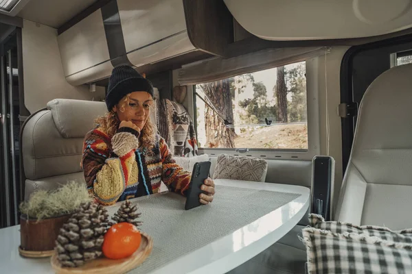 woman living inside a modern camper van motor home sitting at the table and using a mobile phone to stay connected. Roaming connection technology for traveler female people in van life lifestyle