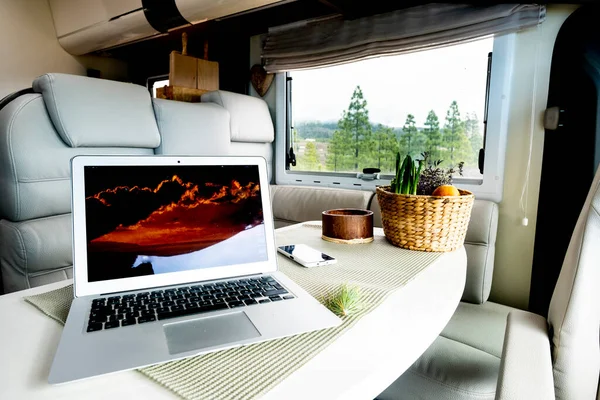 Alternative office and workstation for freedom smart working or digital nomad lifestyle concept. Laptop computer on a motor home table with nature and freedom view outside the window. Job activity