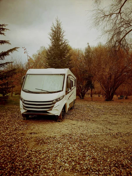 Autumn travel road trip concept with modern camper van parked on the leaves in the woods. Orange mood color old style filter.