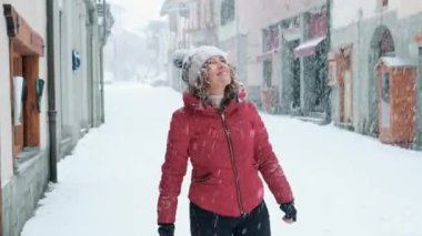 Heyecanlı genç bir kadın, sadece beyaz kış kasabasında kar altında oynayıp dans ediyor. Mutluluk ve neşeli yaşam tarzı. İnsanlar kar ve kış tatilinin tadını dışarıda tatil yaparak çıkarıyorlar.. 