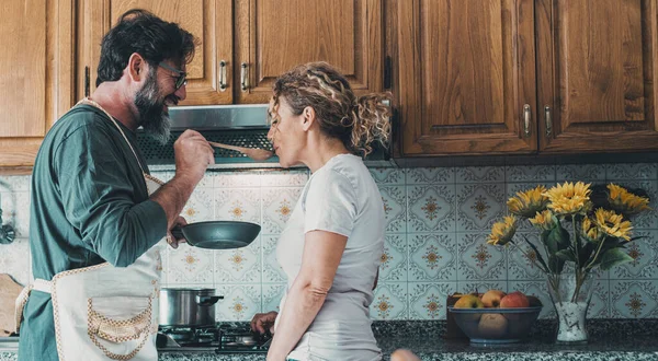 stock image Young mature couple at home in love cooking lunch together. Good relationship in indoor leisure activity together cooking for dinner. Happy man and woman in the kitchen in domestic lifestyle. Romance