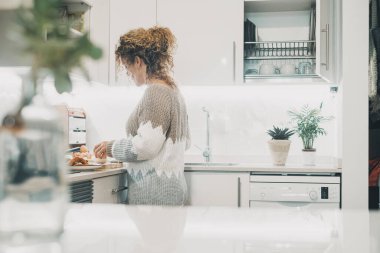 woman alone in the kitchen in real life preparing food for lunch. Single lady lifestyle concept. White home interior minimal style. Indoor leisure activity, cooking for dinner.