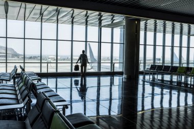  man standing at the airport gate waiting his flight with delay or canceled. Traveler people lifestyle in indoor leisure activity. One tourist with backpack wait to fly with airplane for vacation
