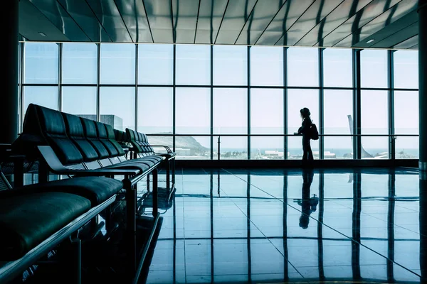 Airport gate and people waiting to fly. Silhouette tourist woman standing and looking outside at the aircraft. People on vacation or business trip. Travel lifestyle and mirror on the floor. Tourism